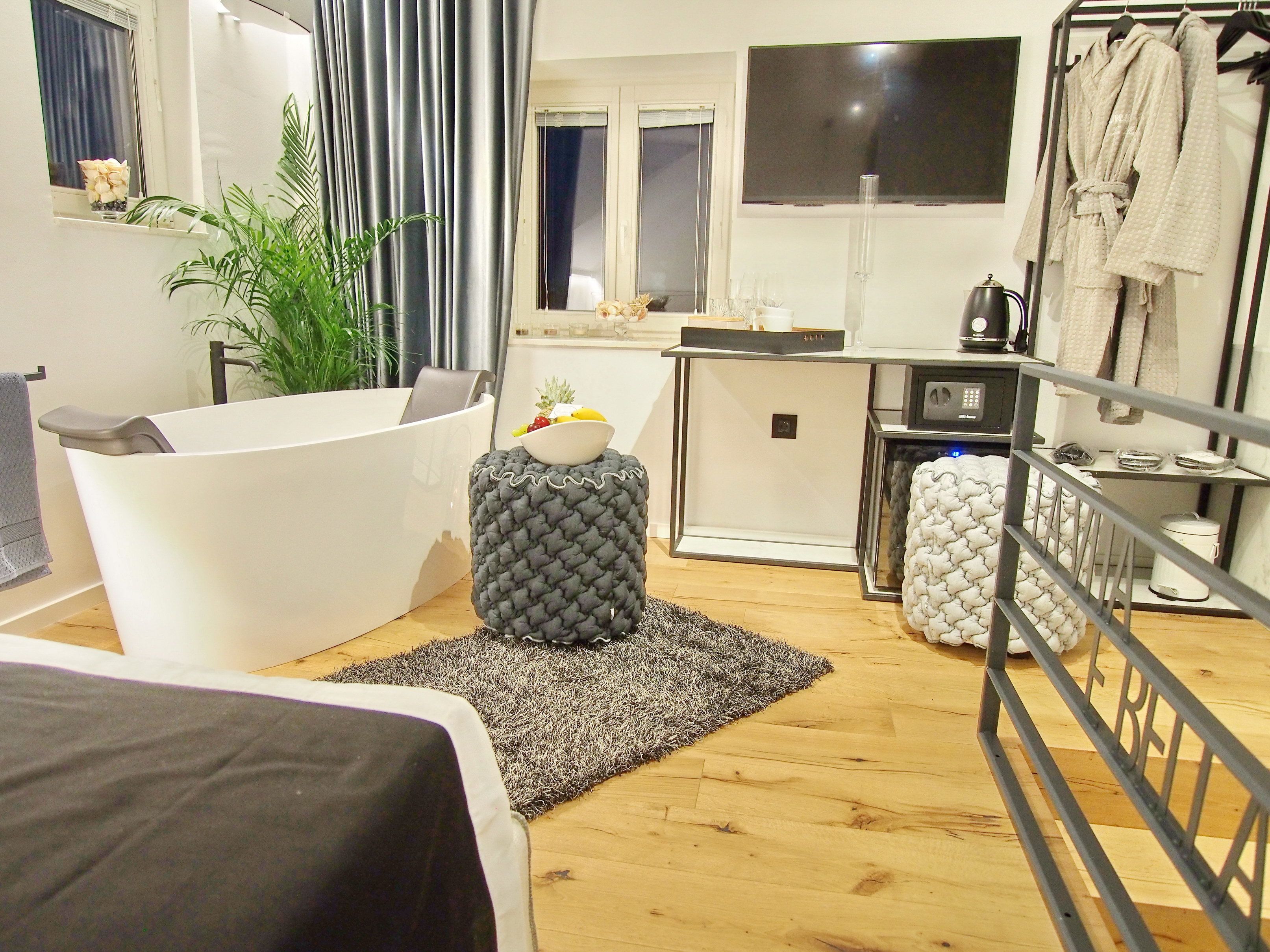 Une chambre d’hôtel compacte au design moderne, dotée d’une baignoire, d’un petit coin cuisine et d’un espace salon avec un canapé et un pouf.