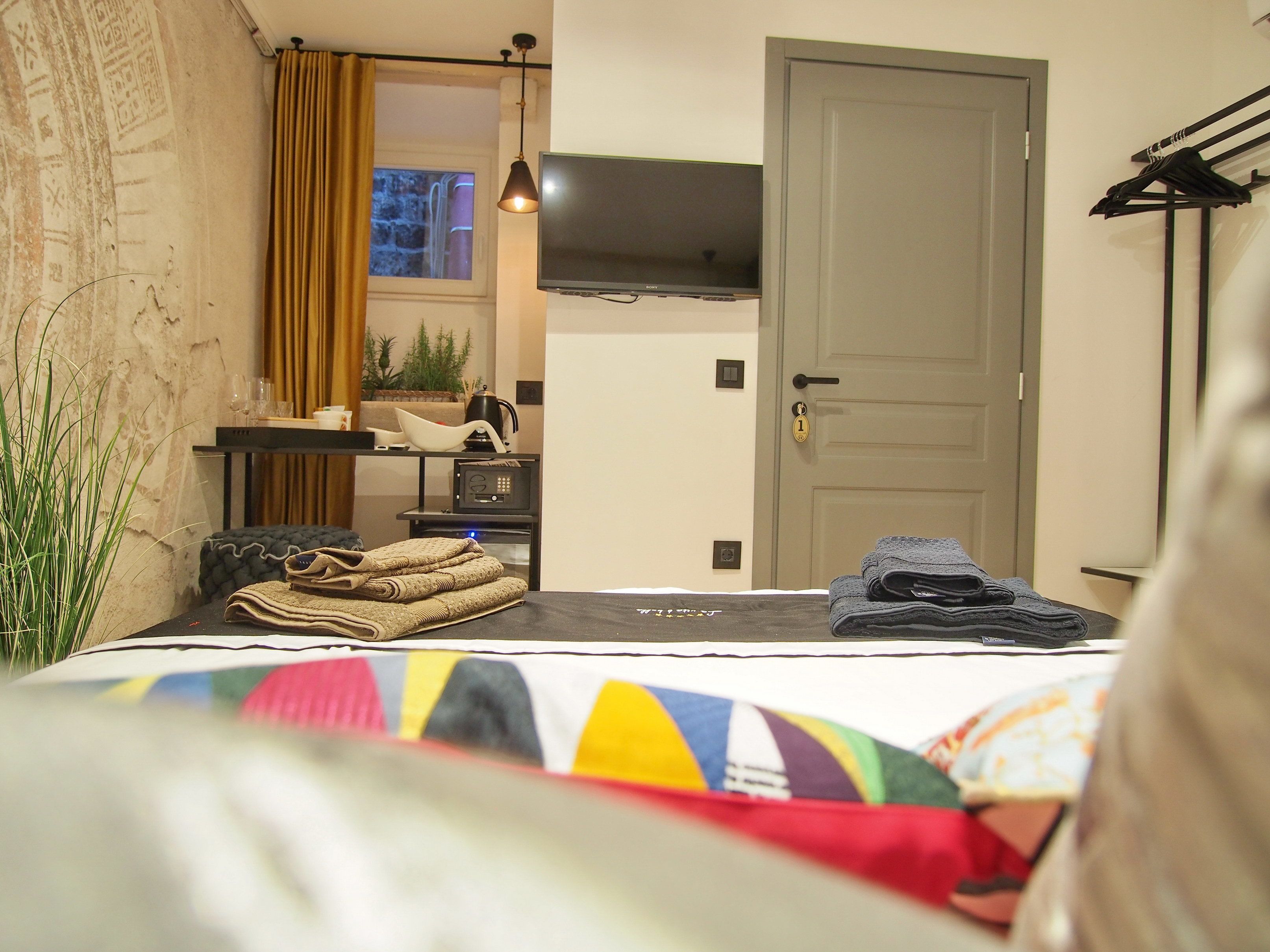 A hotel room with a bed, a desk with a computer, a TV, and a door with a lock.