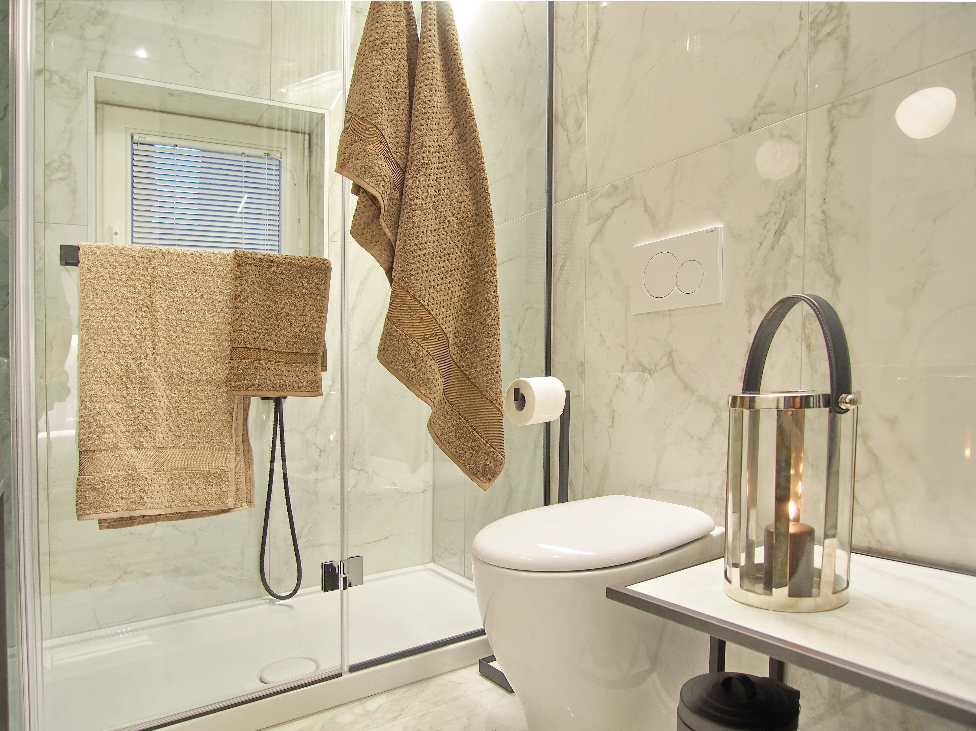 Ein modernes Badezimmer mit Duschkabine aus Glas, einer weißen Toilette und einem Waschtisch mit Glasplatte und Kerzenhalter.