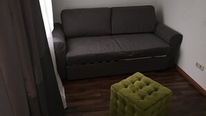 A room with a dark grey sofa and a green ottoman. - Elbsandstein Apartment Altstadt (Erfurt)