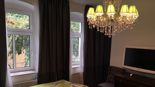 A bedroom with a bed, a TV, a dresser, and a chandelier. - Elbsandstein Apartment Altstadt (Erfurt)
