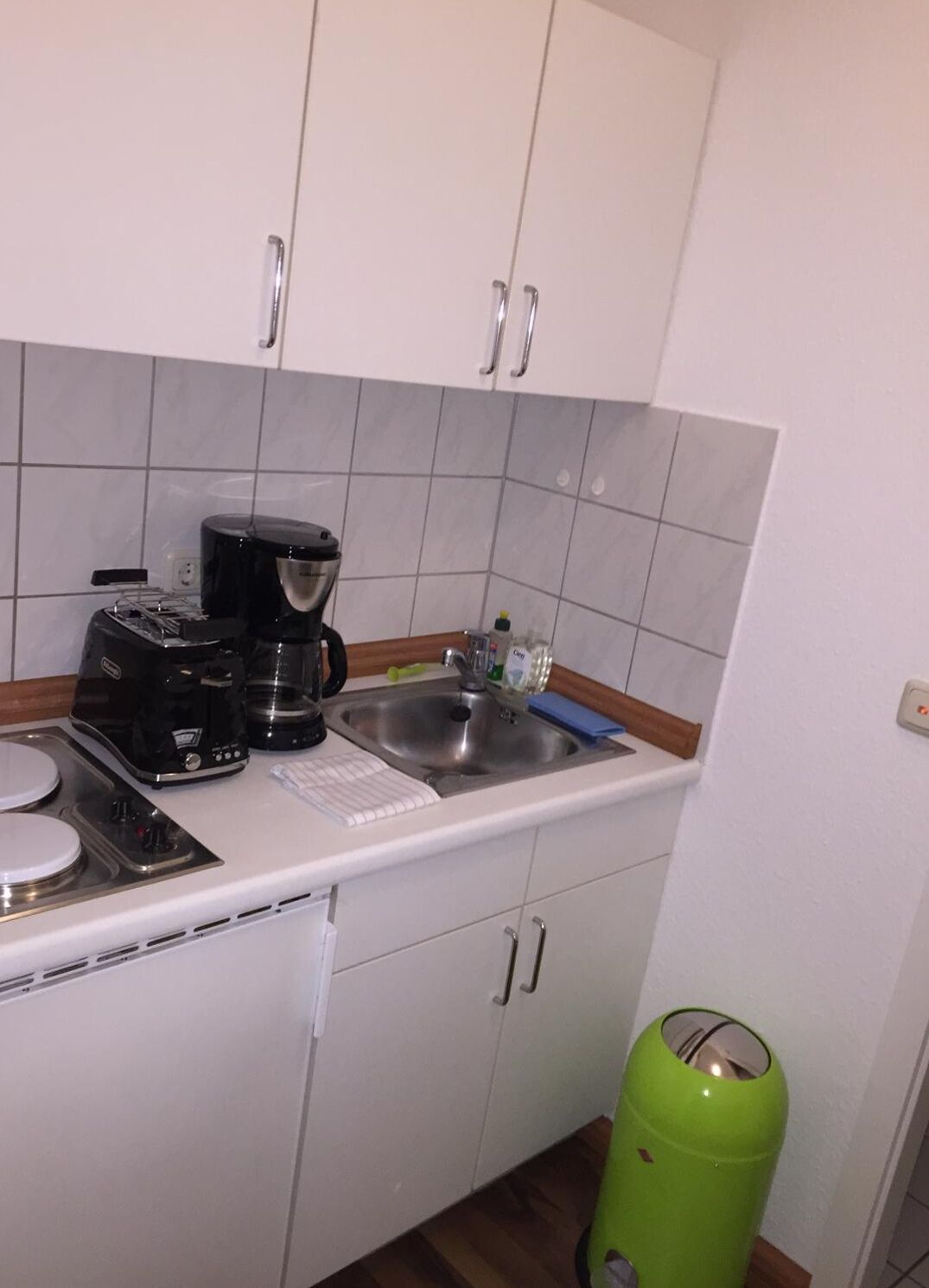 Ett litet pentry med en kaffebryggare, en diskho och en grön soptunna.