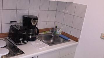 Ett litet pentry med en kaffebryggare, en diskho och en grön soptunna.