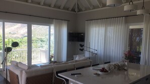 A modern living room with a sofa, a dining table, and a kitchen area with a washing machine. - 2 Bedroom Bungalow-Style Villa (Basseterre)