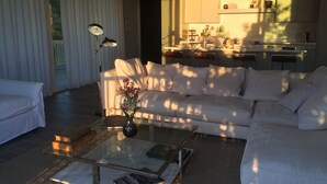 A modern living room with a white sofa, a glass coffee table, and a floor lamp. There is a kitchen area in the background with a dining table and chairs. - 2 Bedroom Bungalow-Style Villa (Basseterre)