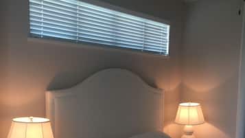 A bedroom with a bed, two bedside lamps, a ceiling fan, and a window with blinds.