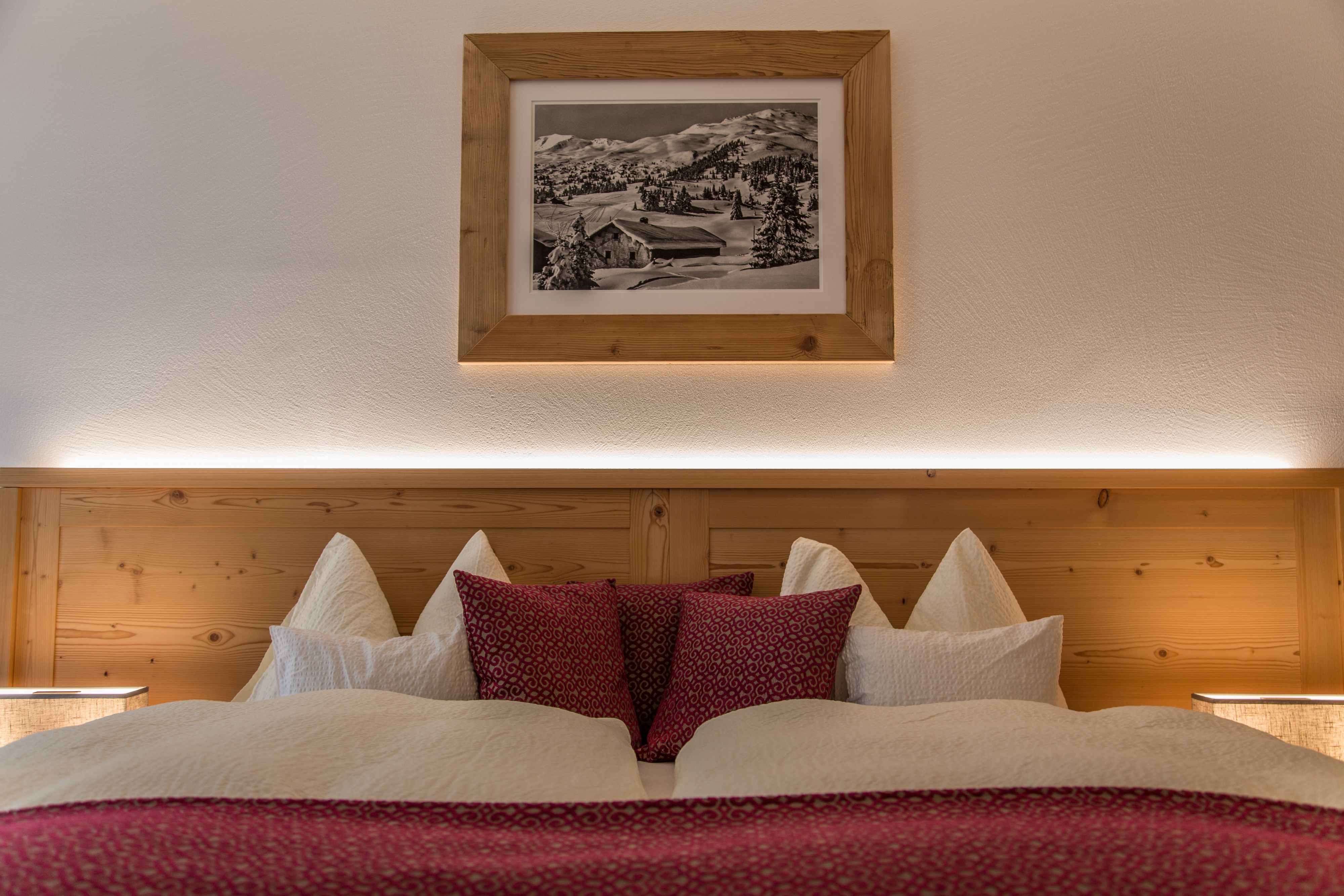 Une chambre à coucher avec une tête de lit en bois, un tableau encadré au-dessus du lit et une couvre-lit rouge à motifs.
