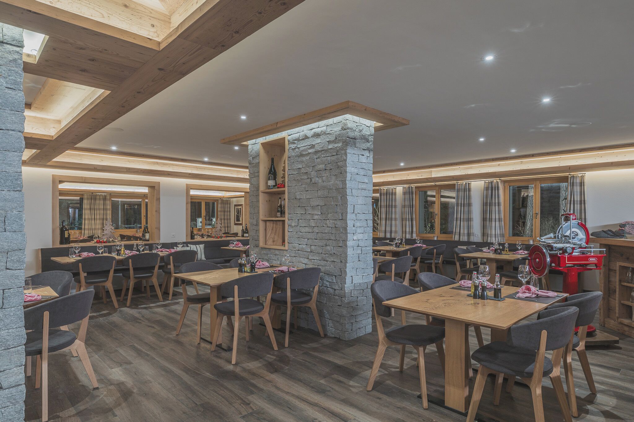 A restaurant with wooden tables and chairs, stone pillars, and a red food preparation station.