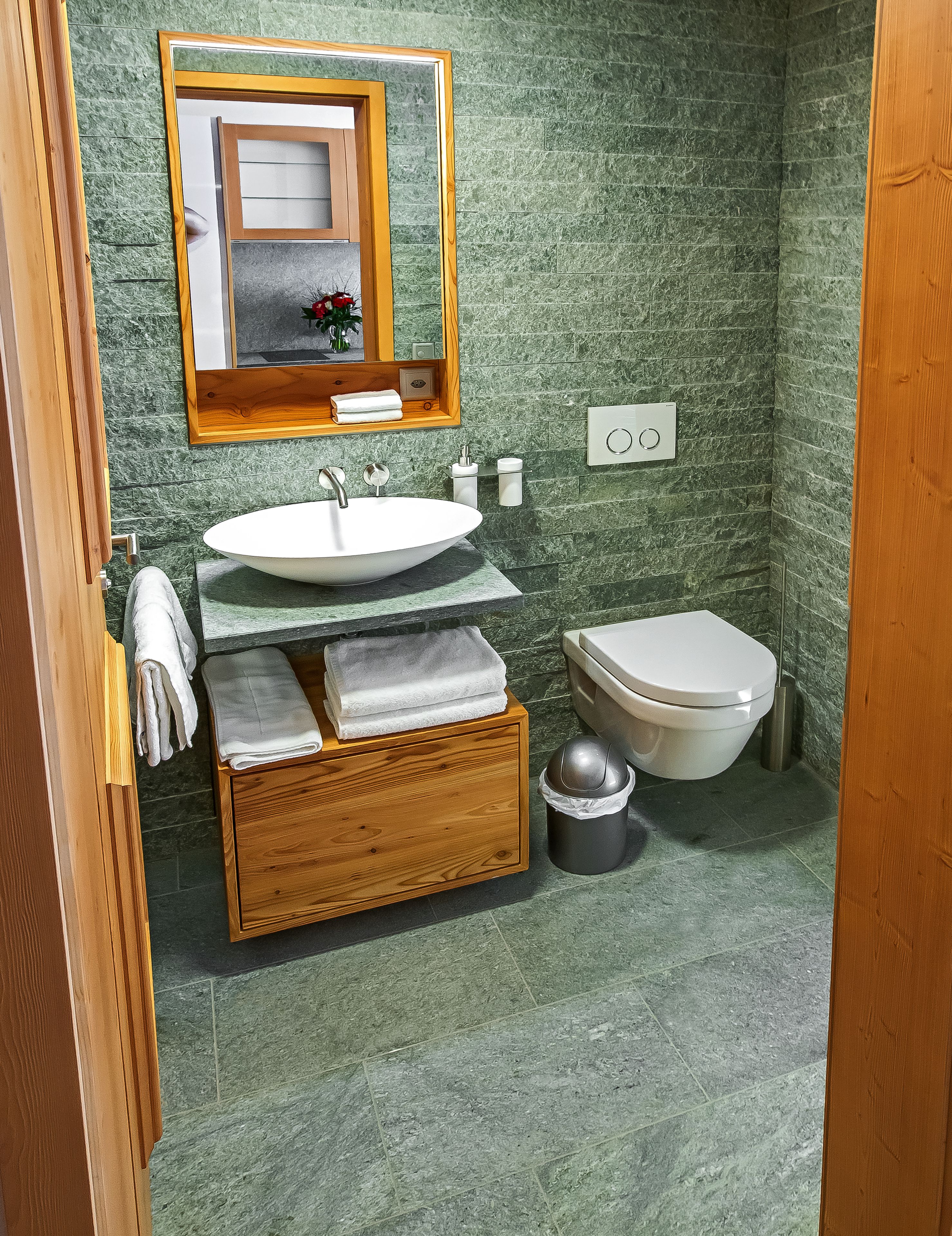 A bathroom with a wooden vanity, a white sink, a toilet, and a mirror above the sink.