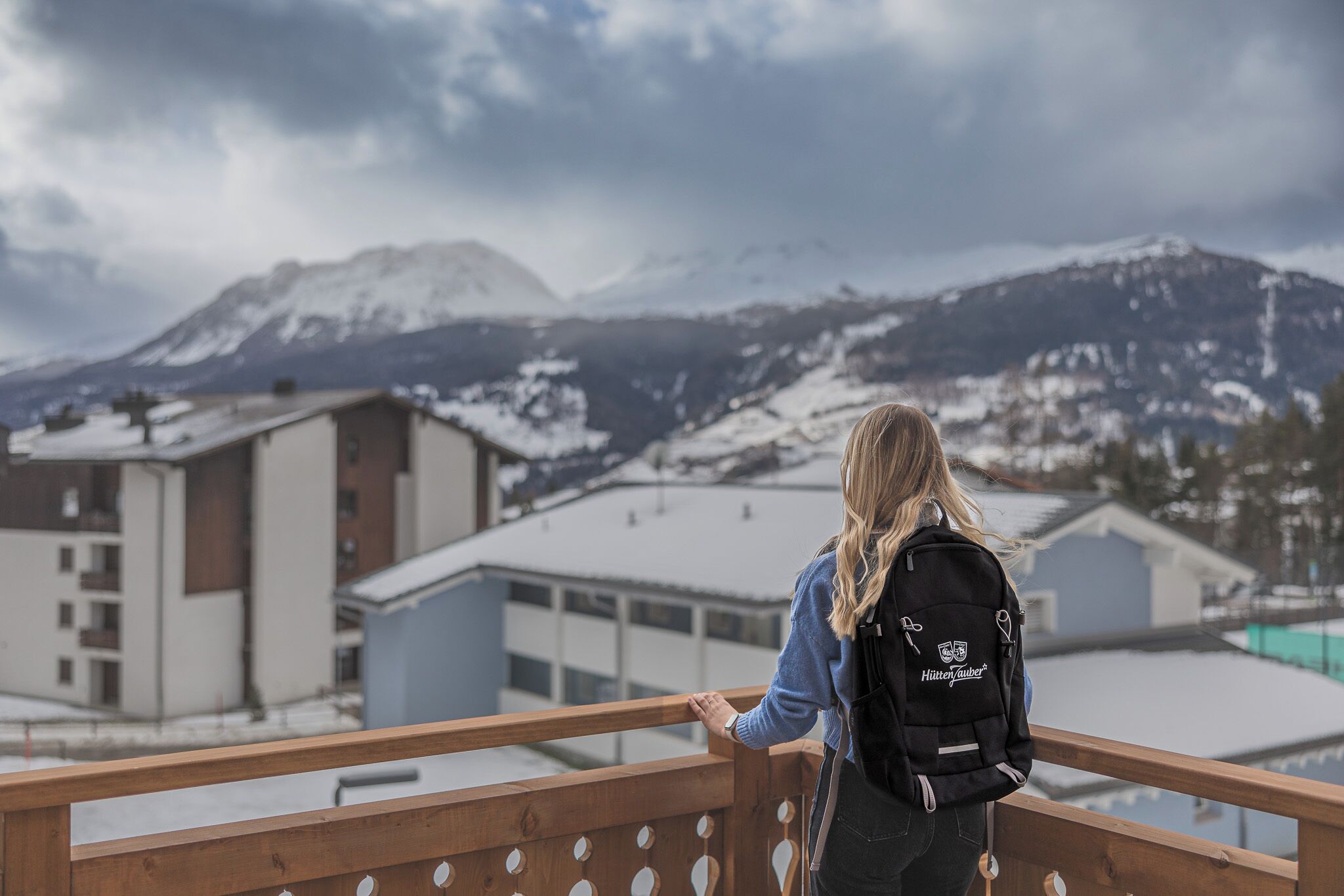 En person med en ryggsäck står på en balkong och blickar ut över ett snötäckt berglandskap.