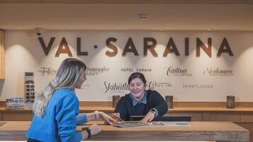 Una recepción con un cartel que dice "VAL-SARINA" y varios nombres de hoteles como "HOTEL SARAIN" y "SPORTLodge".