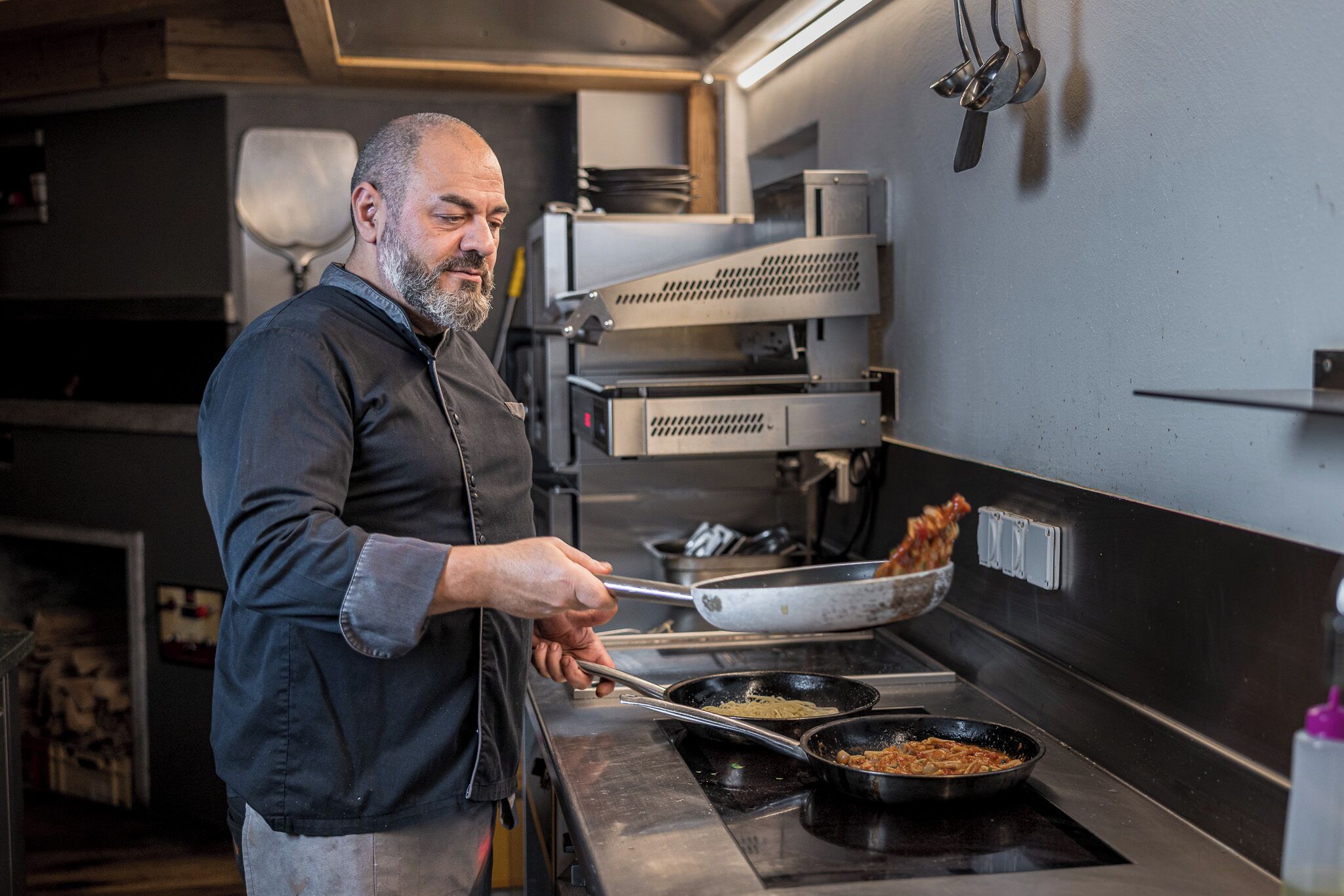A chef cooking in a professional kitchen with stainless steel appliances and a clean, organized layout.