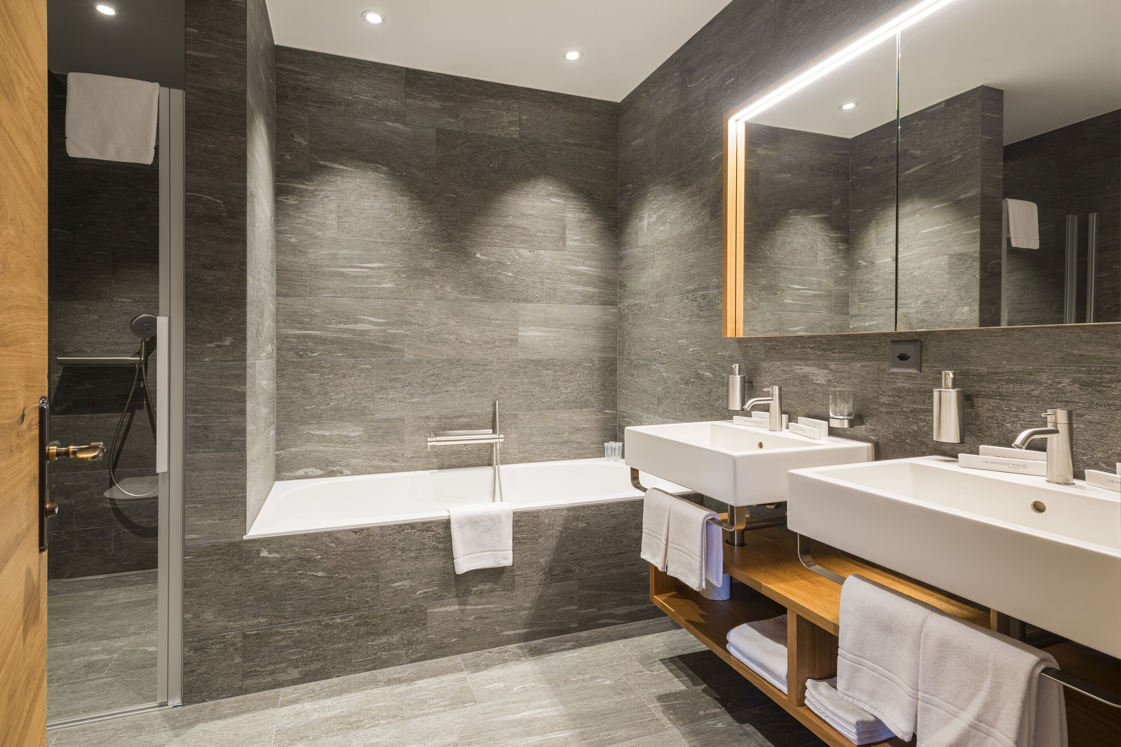 Un baño moderno con un espejo grande, dos lavamanos, una bañera y una ducha.