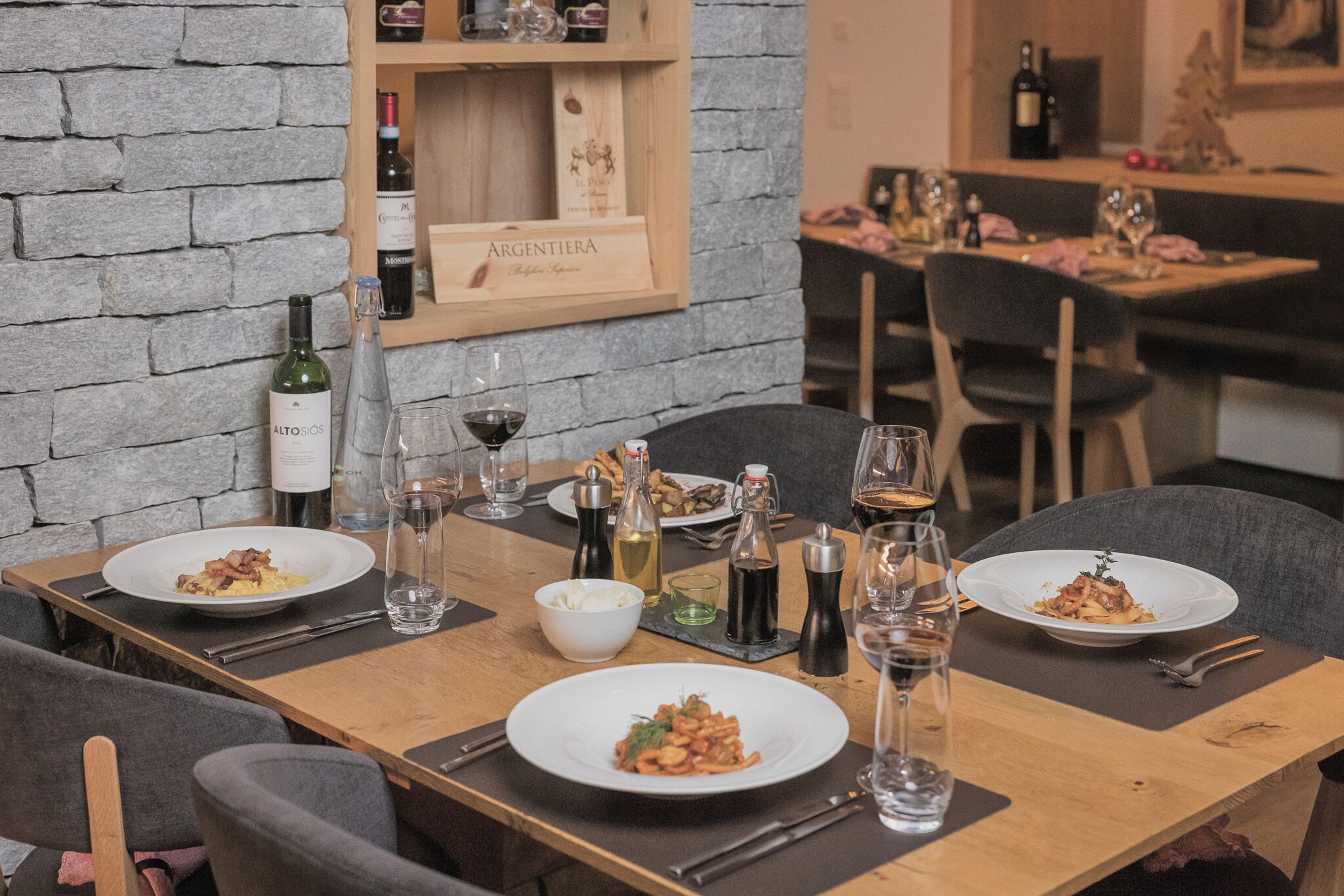 A dining table set with plates of food, wine glasses, and bottles of wine.