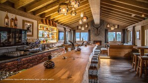 A spacious bar area with wooden beams, a long counter, and a fireplace. - Hotel Sarain - Val Saraina Resort Lenzerheide (Lantsch-Lenz)
