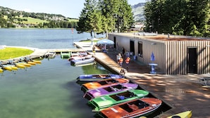 A dock with colorful boats, a wooden building, and a lake with hills in the background. - Hotel Sarain - Val Saraina Resort Lenzerheide (Lantsch-Lenz)