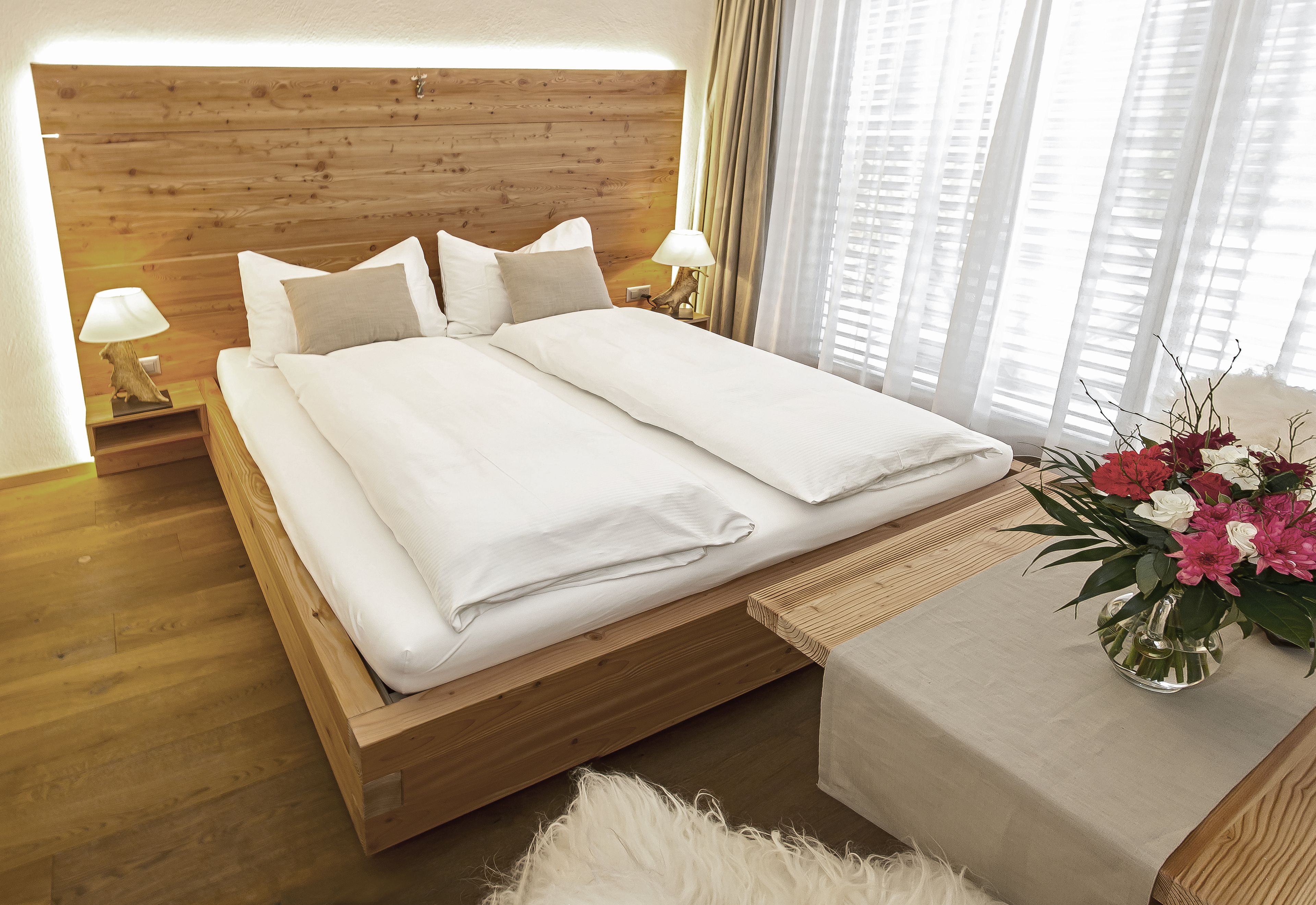 A neatly made bed with white linens, a wooden headboard, and a bedside table with a lamp.