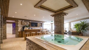 A spa area with a hot tub, wooden bar, stone walls, and a television. - Hotel Sarain - Val Saraina Resort Lenzerheide (Lantsch-Lenz)