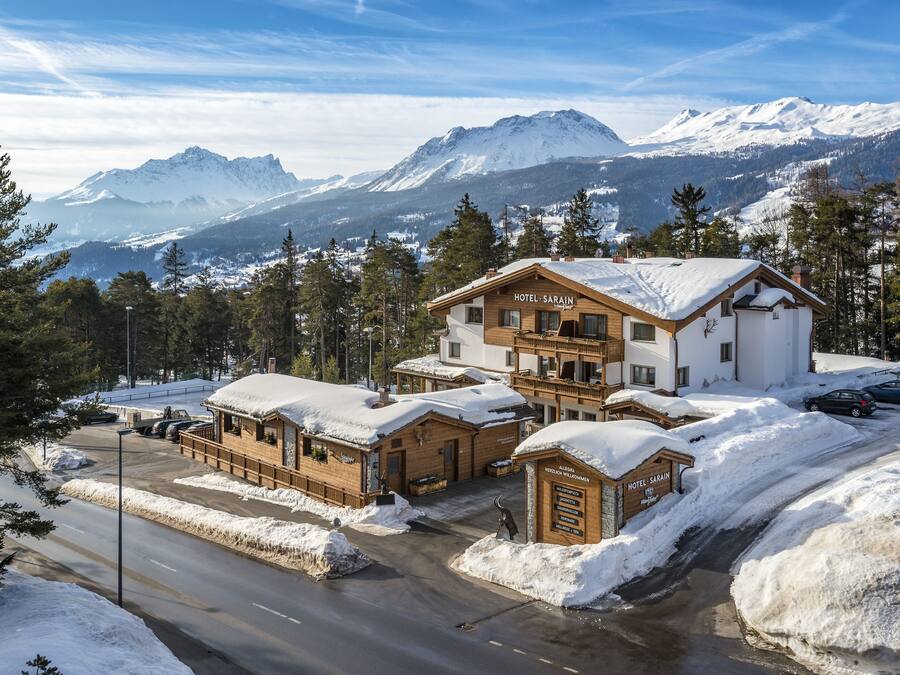 A hotel with a snow-covered roof, a wooden facade, and a view of snow-capped mountains in the background.