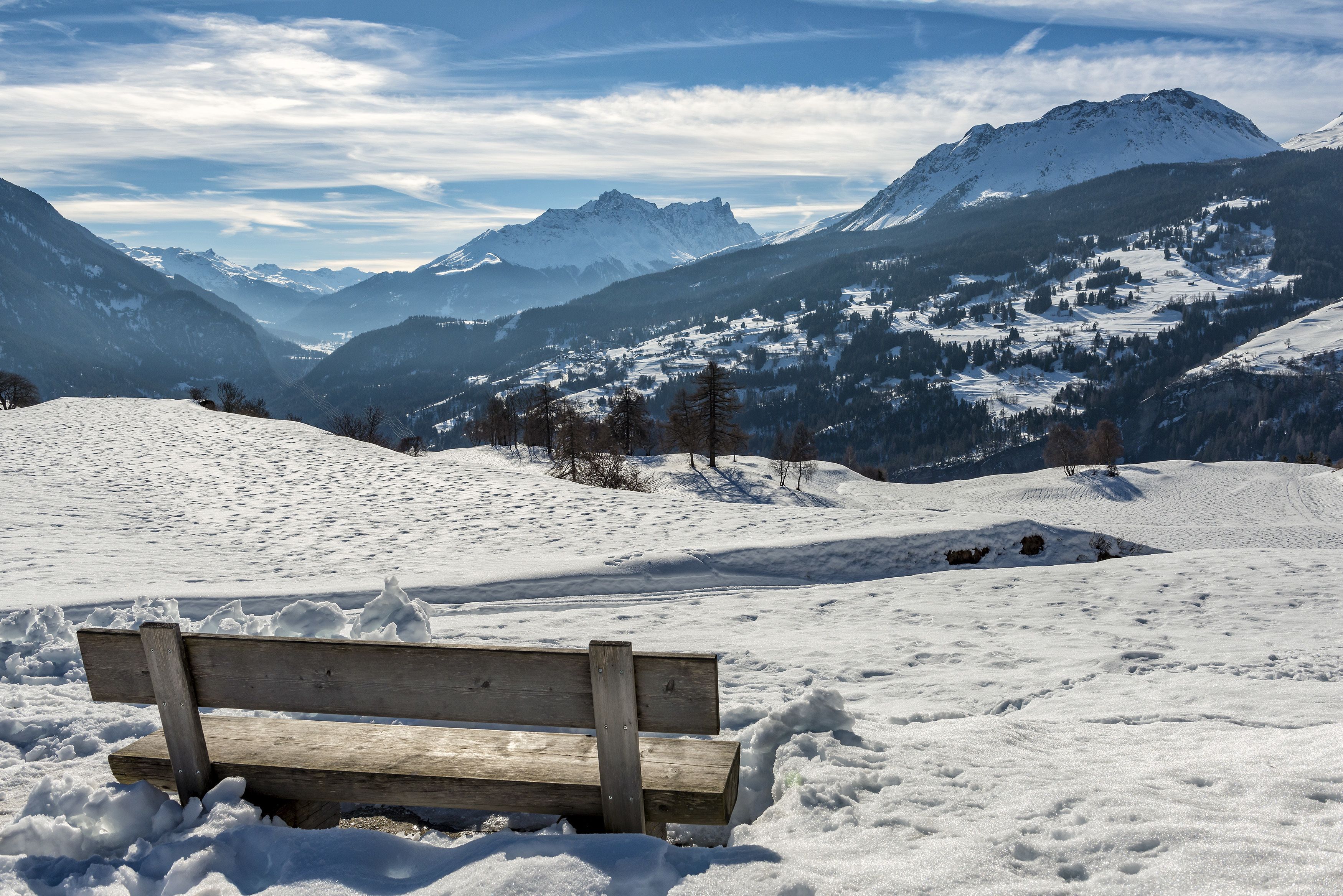 Un banc en bois dans un paysage enneigé, avec des montagnes en arrière-plan.