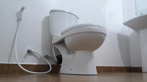 A white toilet with a tank and a bidet attachment, connected to a wall-mounted pipe. - Akila Holiday Resort (Avudangawa)