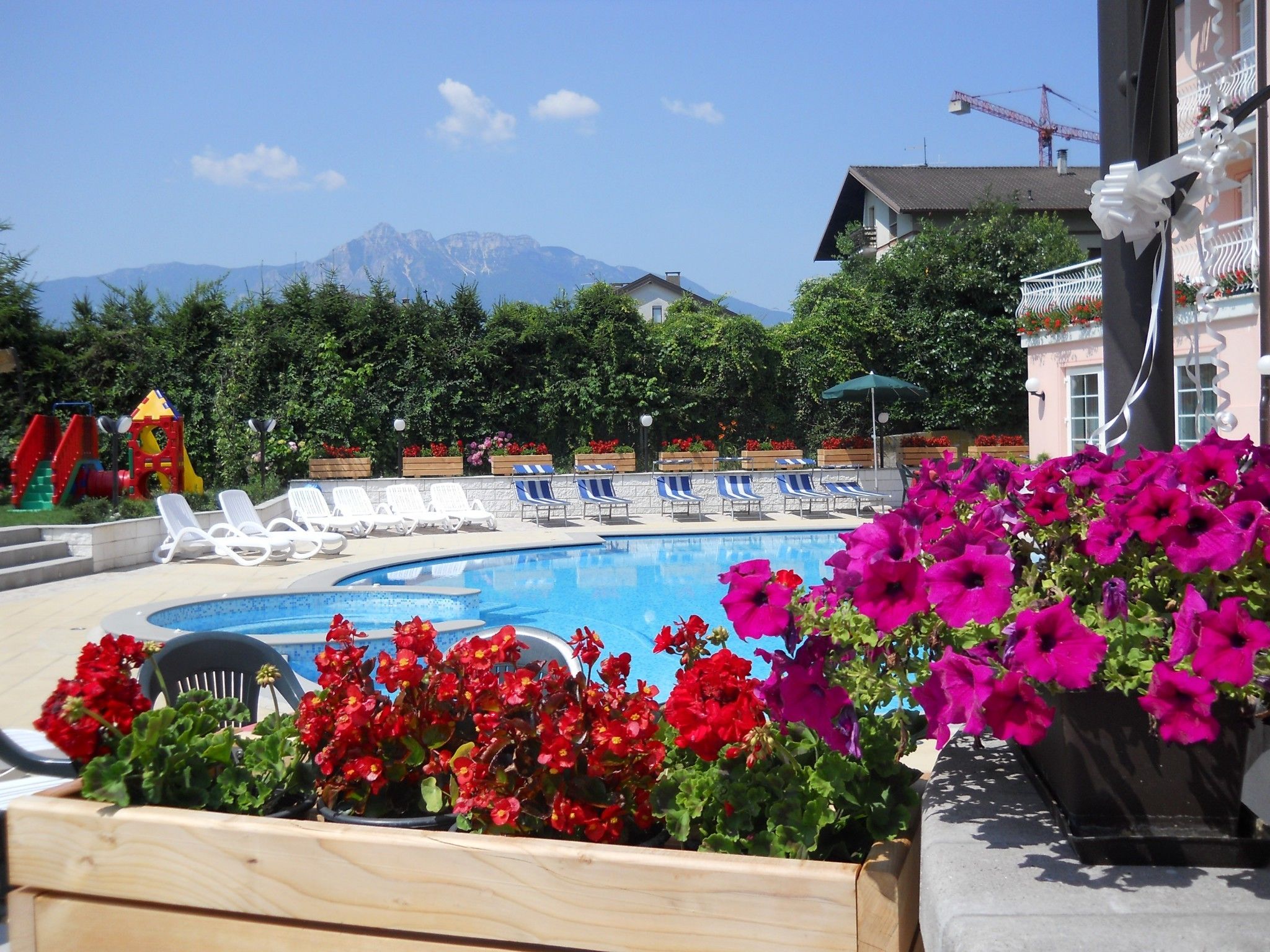 A pool area with lounge chairs, a children's play structure, and a mountain view.