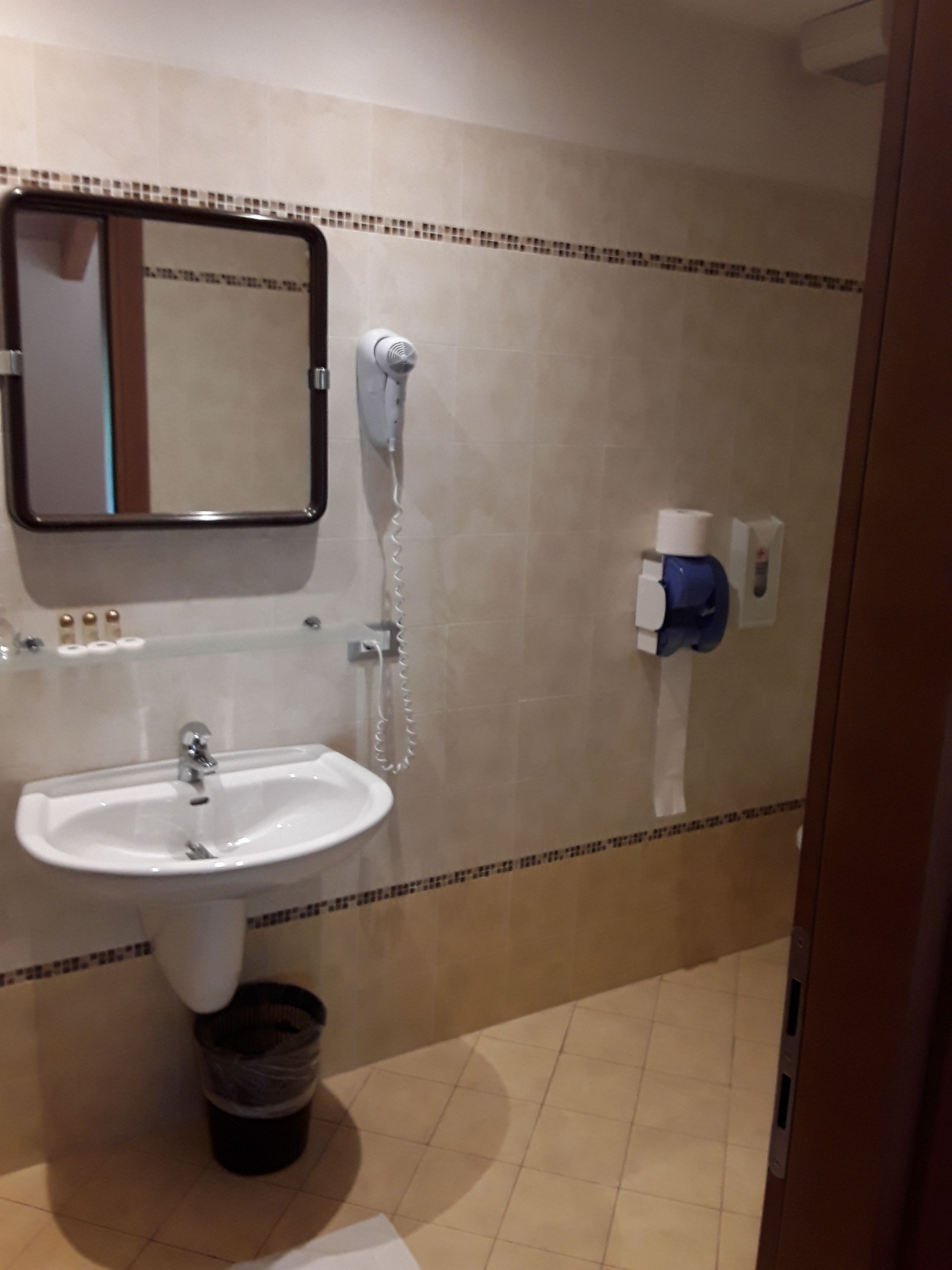 Un baño con lavamanos, espejo, secador de pelo y dispensador de toallas.