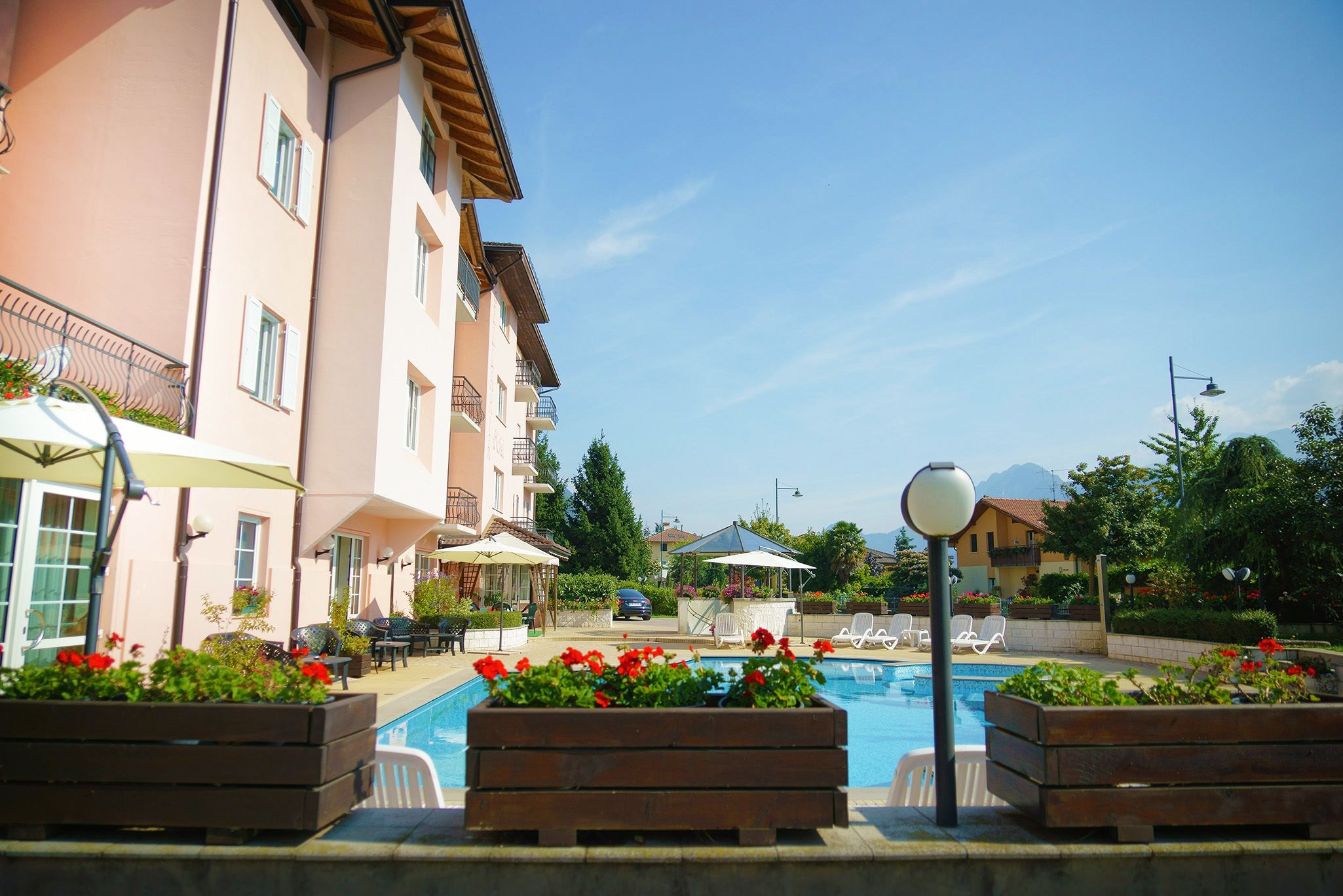 Area piscina con lettini, fioriere in legno e un edificio con balconi.