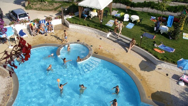 A swimming pool with multiple people enjoying the water, surrounded by lounge chairs and umbrellas. - Hotel Bellaria (Levico Terme)