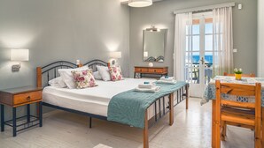 A bedroom with a bed, bedside tables, a dresser, a mirror, a window with curtains, and a view of the sea. - Porto Giardino Apartments (Zakynthos)