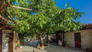 A courtyard with a large tree, stone walls, and potted plants. - Porto Giardino Apartments (Zakynthos)