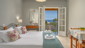 A bedroom with a bed, a dresser, a mirror, and an open door leading to a balcony with a table and chairs. - Porto Giardino Apartments (Zakynthos)