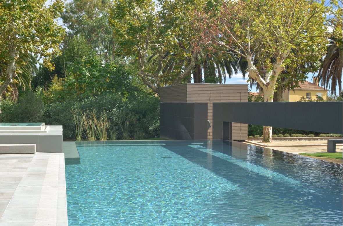 A modern outdoor swimming pool with clear water, surrounded by lush greenery and a contemporary building structure.