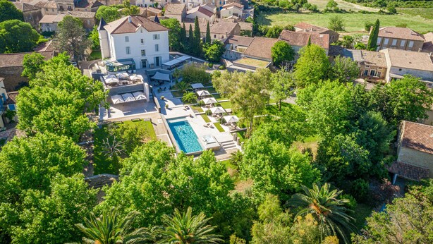 An aerial view of a residential area with a large white house, a swimming pool, and surrounding greenery. - Château Autignac (Autignac)