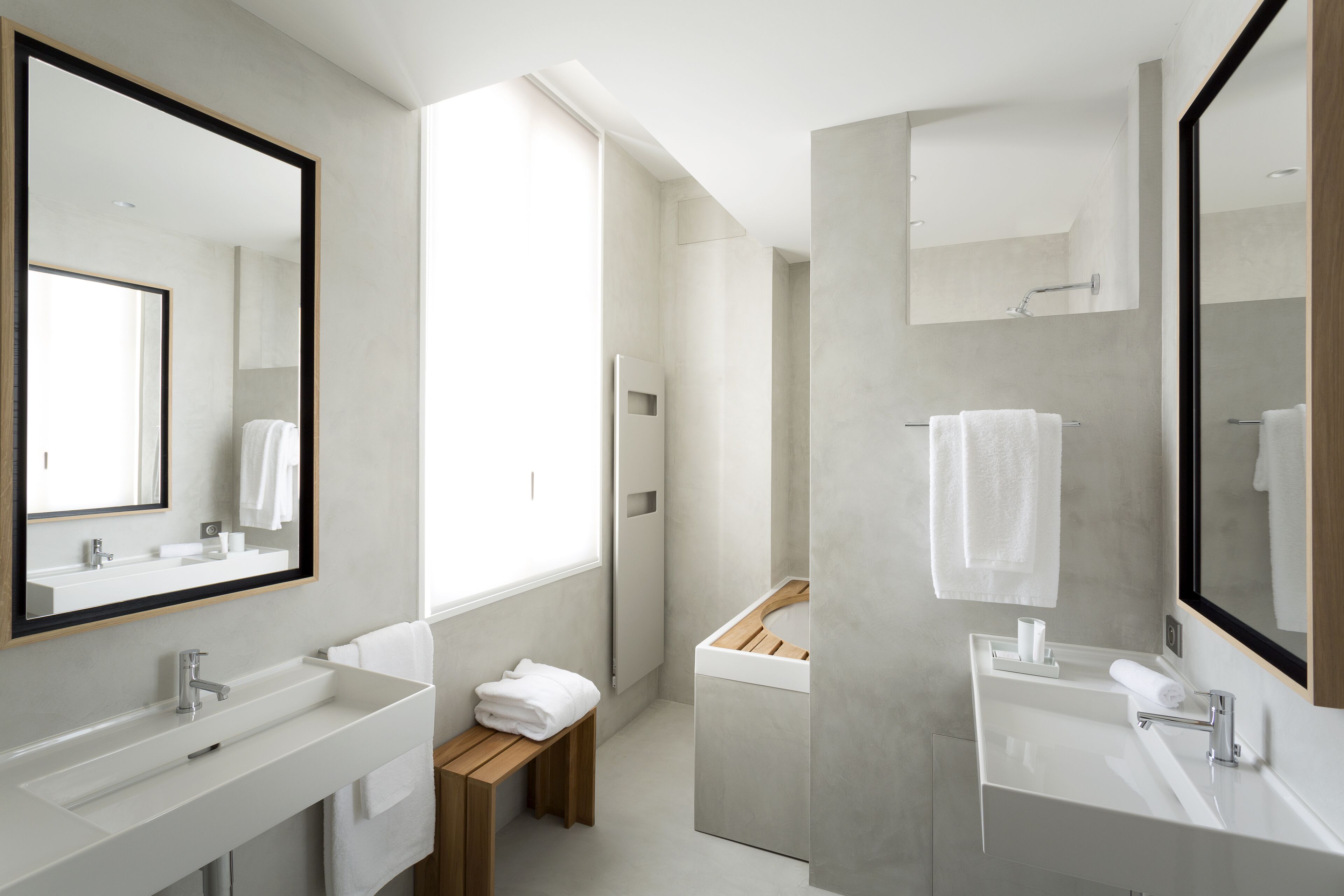 A modern bathroom with two sinks, a wooden bench, and a large mirror.