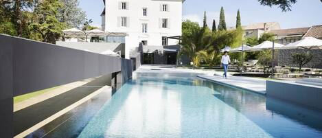 Una piscina de diseño moderno, rodeada de jardines y un edificio grande al fondo.