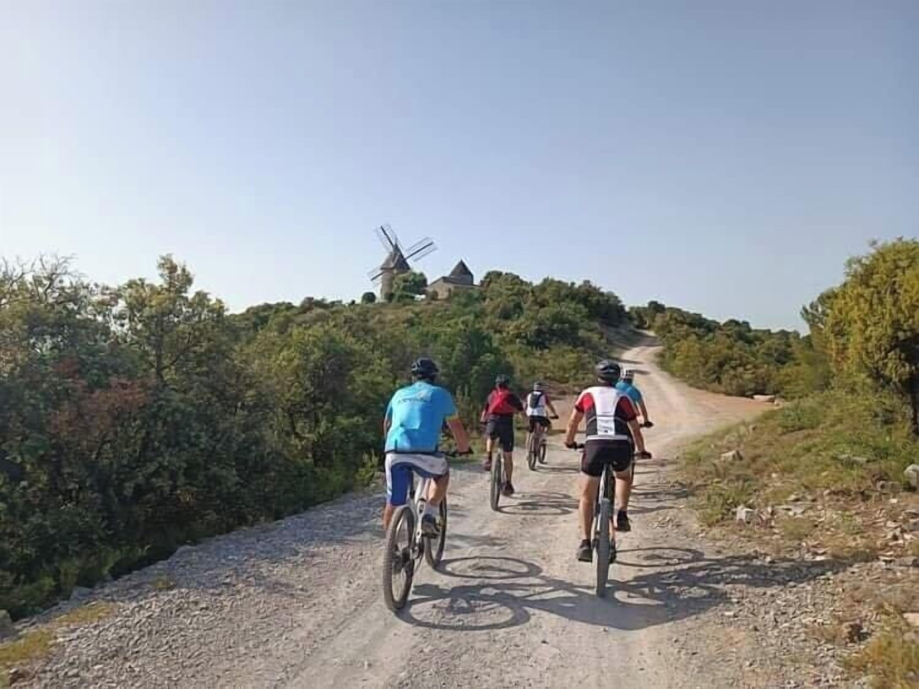 Um grupo de ciclistas em uma trilha de terra com um moinho de vento ao fundo.