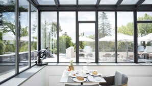 A dining area with a table set for breakfast, large windows, and outdoor seating visible through the glass. - Château Autignac (Autignac)