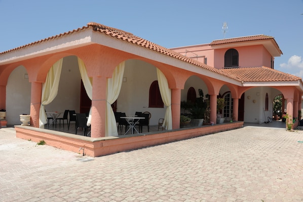 Un bâtiment doté d’un toit en tuiles, d’une cour ouverte avec un sol pavé et d’un espace de repos couvert, équipé de tables et de chaises.