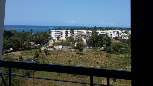 Blick von einem Balkon auf eine Küstenlandschaft mit weißen Gebäuden, viel Grün und dem Meer.