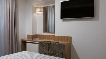 Una habitación de hotel con cama, escritorio, silla, televisión y ventana con cortinas.