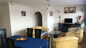 Un espace de vie compact comprenant une table à manger, deux canapés, un téléviseur et un petit coin cuisine.