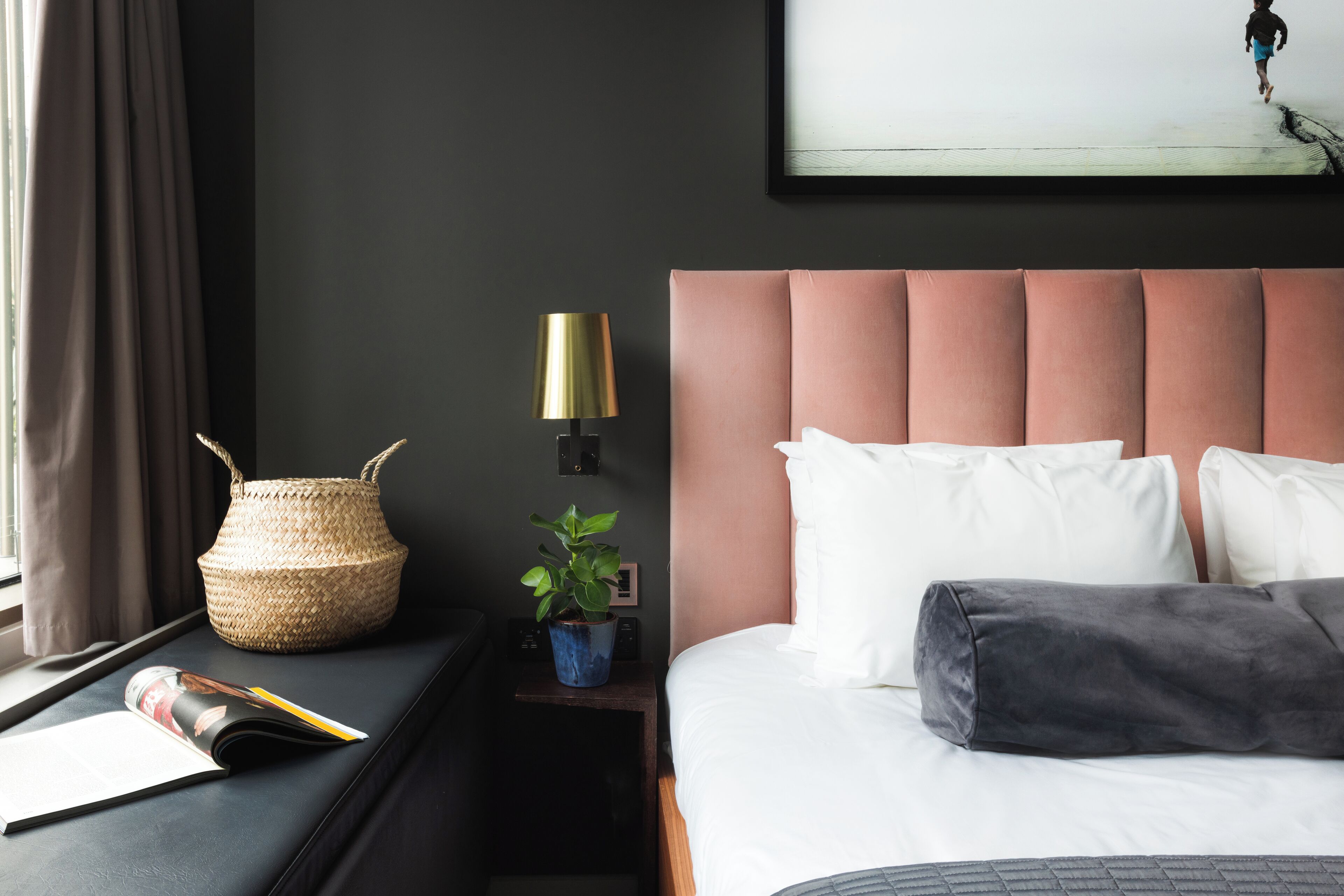 Habitación de hotel ordenada con cama, mesita de noche, lámpara y un cuadro colgado en la pared.