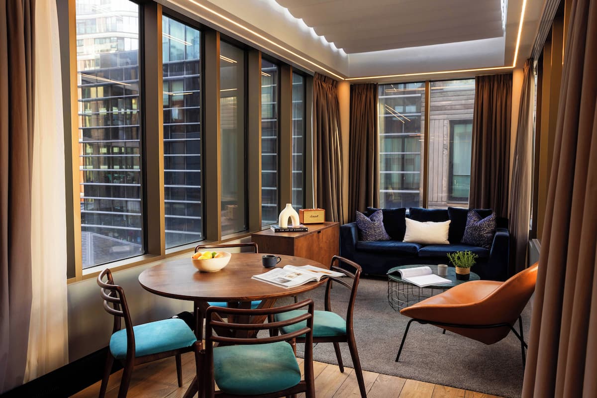 Quarto de hotel moderno com área de refeições, um sofá e vista para a cidade.