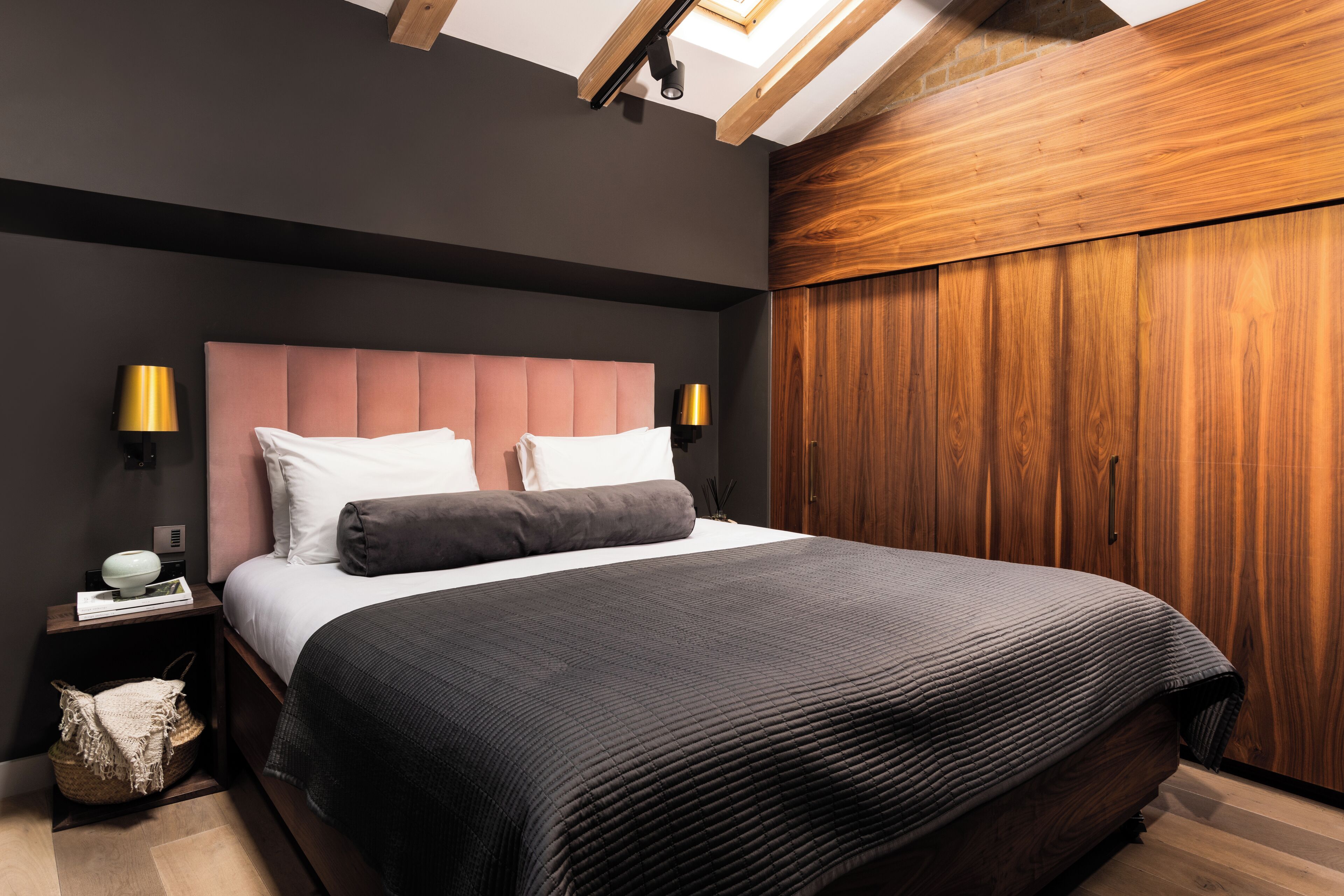 A modern bedroom with a large bed, dark walls, wooden paneling, and two bedside lamps.