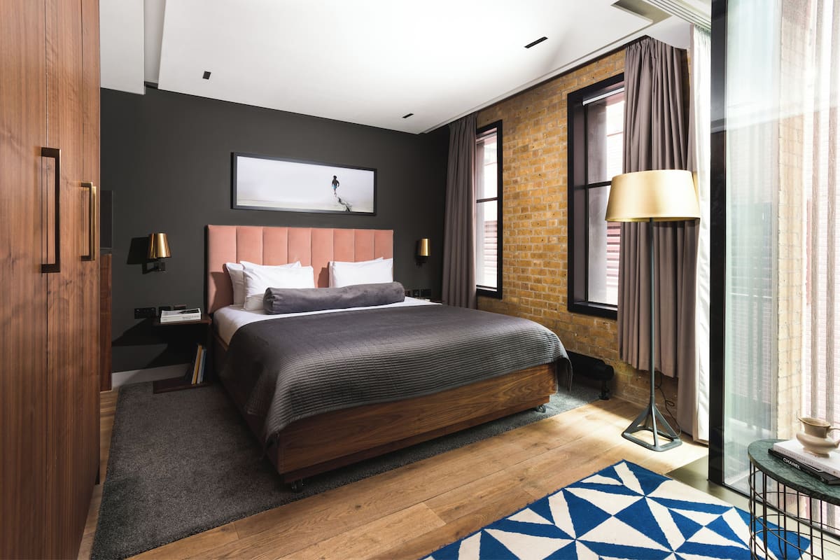 Quarto moderno com uma cama grande, parede de tijolos e vista da cidade através de uma janela ampla.