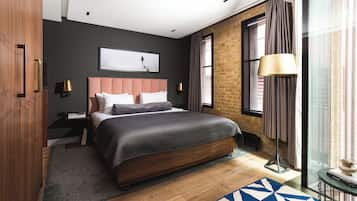 A modern bedroom with a large bed, a brick wall, and a view of the city through a large window.