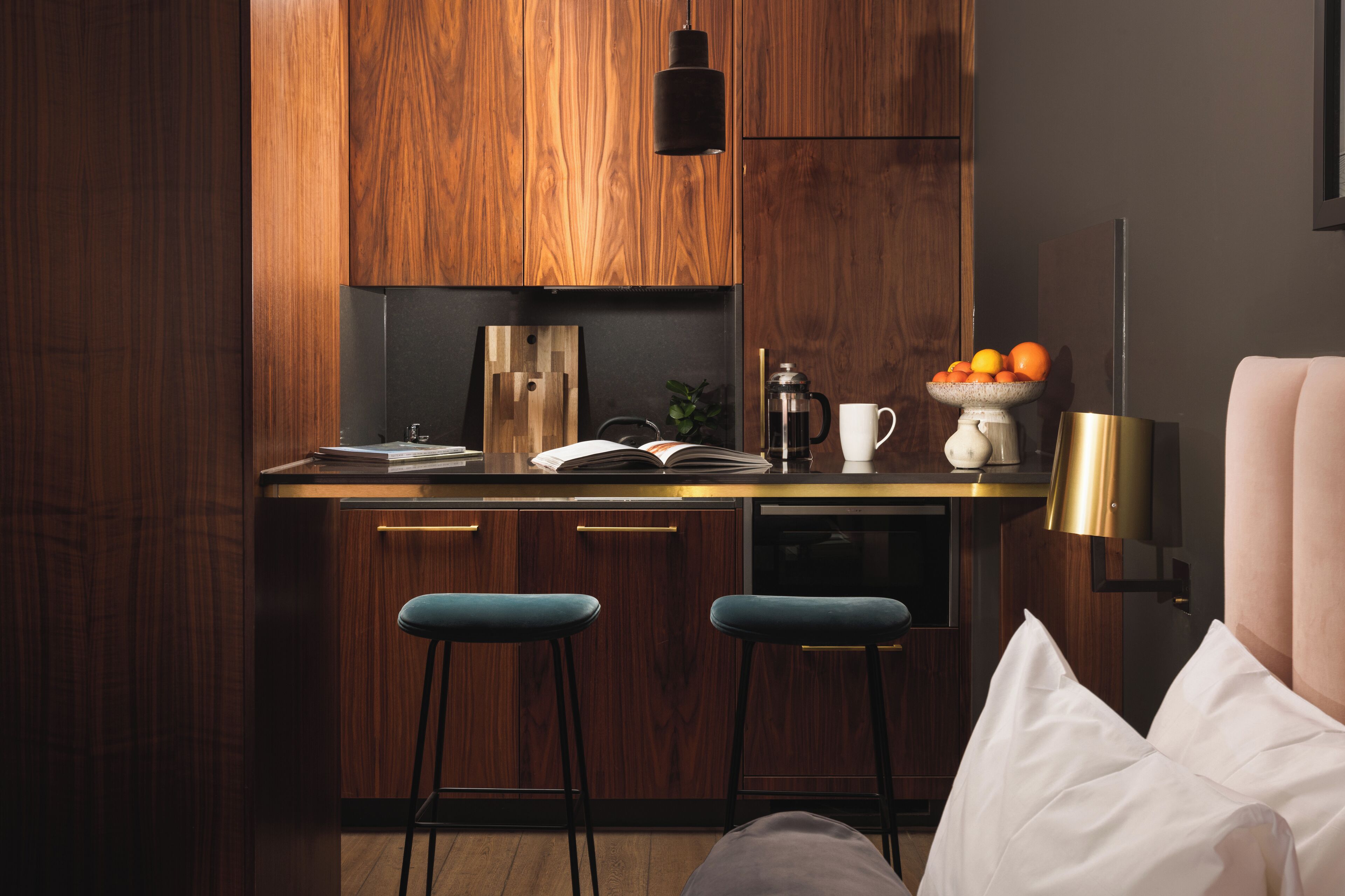 A modern kitchen with wooden cabinets, a bar stool, a coffee maker, and a fruit bowl.