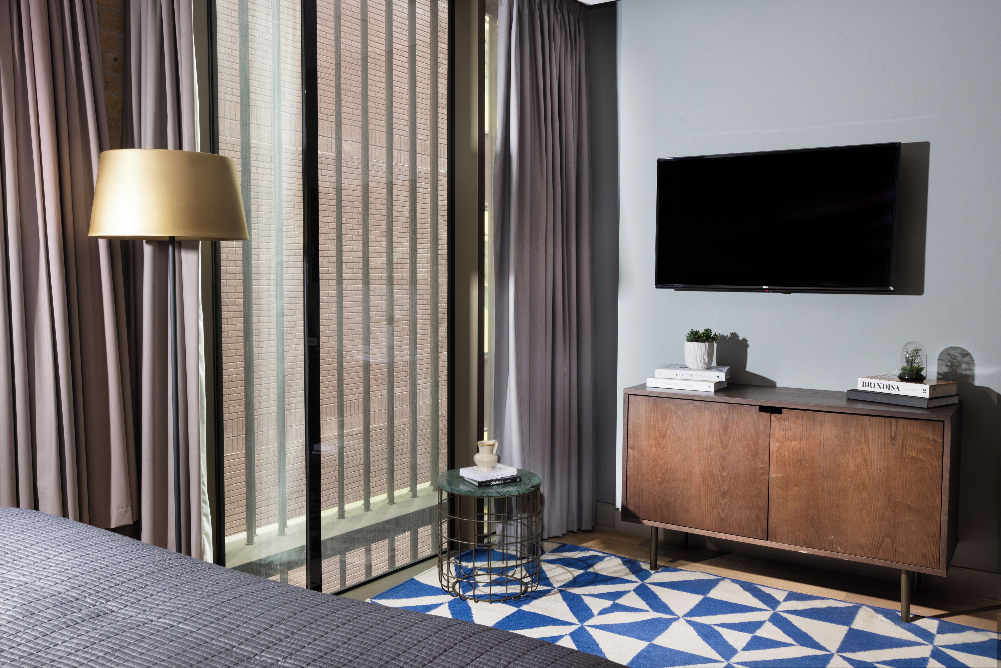Een moderne hotelkamer met een groot bed, een aan de muur bevestigde televisie, een houten kast en een vloerkleed met een geometrisch patroon.