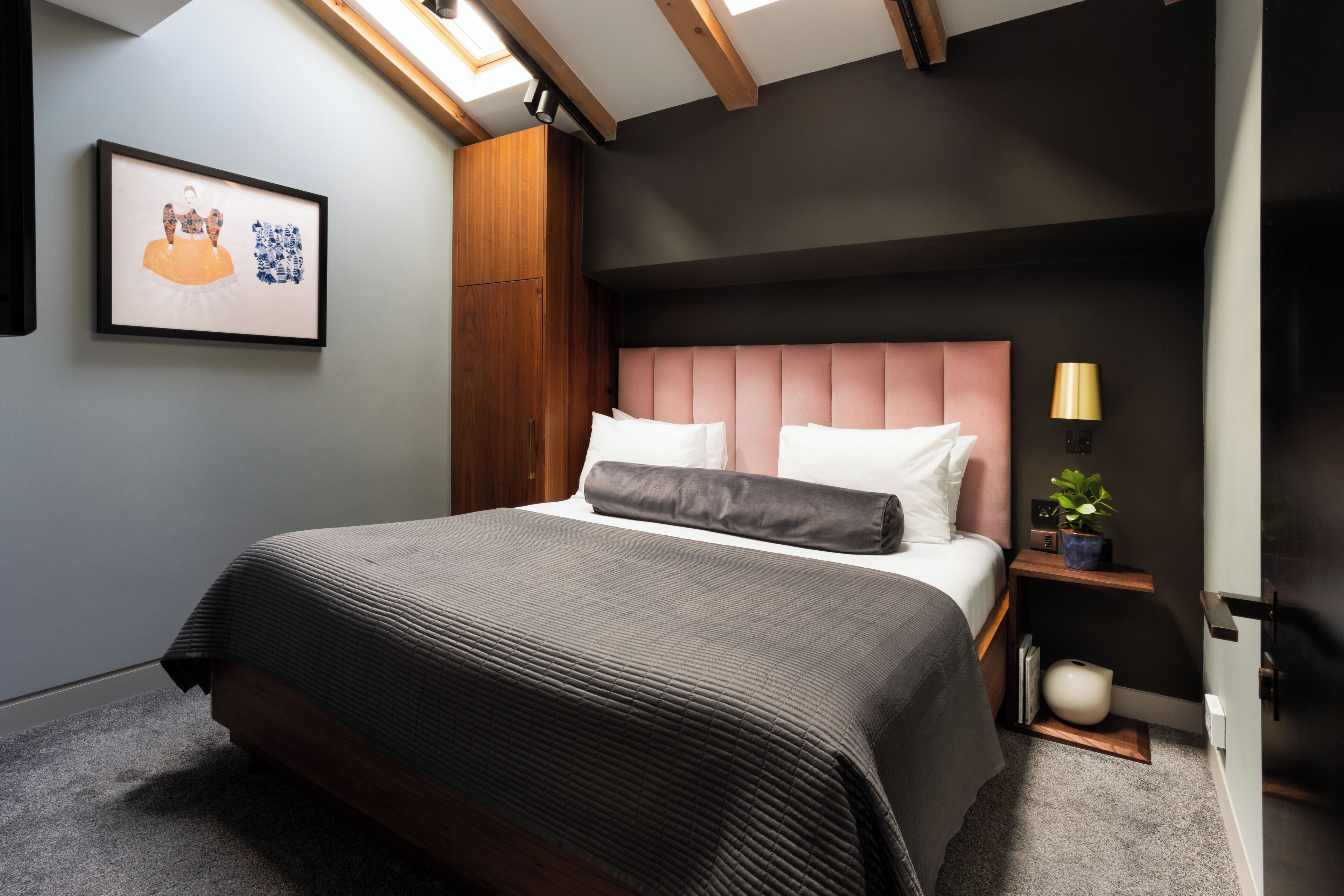 A modern bedroom with a large bed, a headboard, a bedside table with a lamp, and a framed picture on the wall.